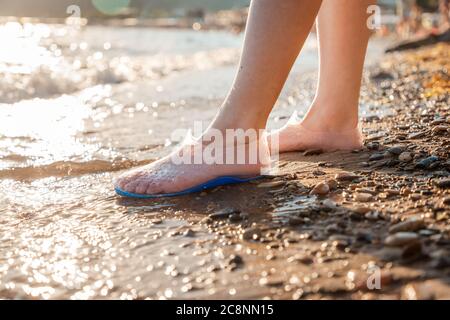 Eine Frau steht in Gummischuhen zum Schwimmen am Strand. Nahaufnahme der Füße. Das Konzept des Schutzes und der Gesundheit der Füße. Stockfoto