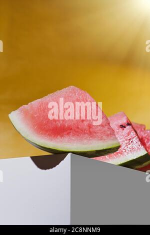 Auf dem weißen Würfel liegen Scheiben reifer Wassermelone. Gelber Hintergrund Stockfoto
