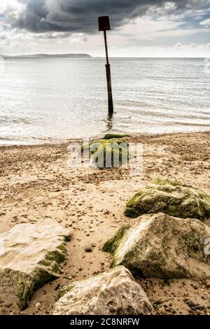 Wellen schlagen über die Felsen eines Groynes am Avon Beach Christchurch mit der Isle of Wight im Hintergrund Stockfoto