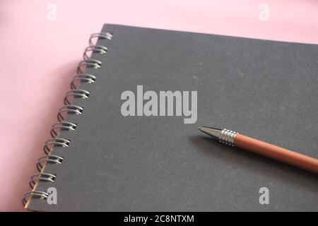 Schwarzer Notizblock mit Stift auf rosafarbenem Tisch. Design-Vorlage mit Copyspace Stockfoto