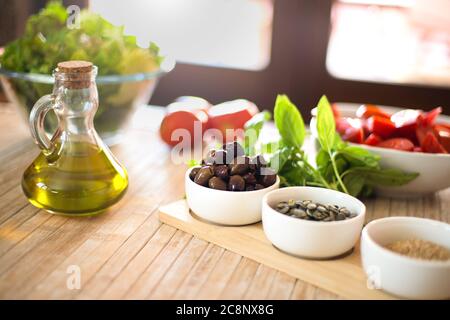 Natives Olivenöl extra und Oliven im Vordergrund mit frischem Gemüse und Sonnenlicht im Hintergrund - mediterranes Diät-Konzept - gesunder Sommer Stockfoto