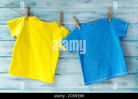 Zwei helle Baby-T-Shirts, die auf einer Wäscheleine auf einem blauen Holzhintergrund hängen Stockfoto