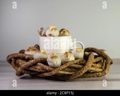 Cappuccino-Kuchenbällchen, trüffelartig, mit Espressopulver bestreut auf einem Holzkranz sitzend mit einem weißen Kaffeebecher in der Mitte. Dessertball Stockfoto