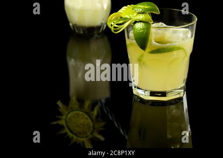 CAIPIRINHA VON ZITRONE EIN TYPISCH BRASILIANISCHES GETRÄNK, FOTOGRAFIERT AUF EINEM DUNKLEN GLASTISCH Stockfoto