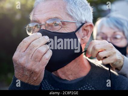 Aktives Seniorenpaar auf Spaziergang im Freien mit Gesichtsmasken. Frau hilft Mann mit Maske. Stockfoto