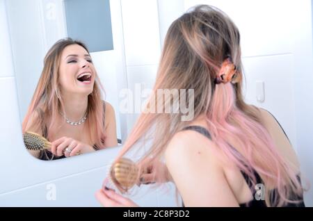 Frau, die im Badezimmer vor dem Spiegel stand. Junge Frau lachend und putzt sich die Haare. Stockfoto