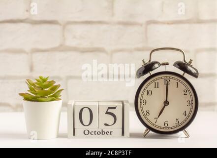 5. Oktober auf dem Holzkalender neben dem Wecker, das Datum des Herbstmonats. Stockfoto