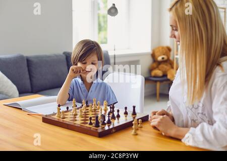 Hobbys für die Familie. Junge Mutter spielt Schach mit Sohn zu Hause. Kleiner Junge in Brettspiel mit seinen Eltern im Zimmer engagiert Stockfoto