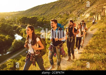 Junge Leute mit Rucksäcken wandern auf schmalen Wegen in den Bergen. Gruppe von fröhlichen Touristen Wandern im Freien im Sommer Stockfoto