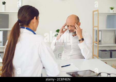 Kopfschmerzen. Der Patient senor teilt dem Arzt mit, dass Kopfschmerzen Symptome auf einem Stuhl in einer Klinik auftreten. Stockfoto