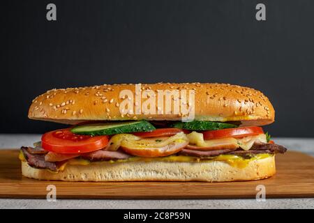 Sandwich mit Sesambrötchen, Käse, Schinken, frischem Gemüse und Senf Stockfoto