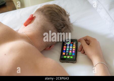 Ein Teenager Junge liegt im Bett und schläft mit seinem Handy Stockfoto