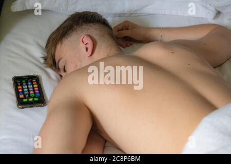 Ein Teenager Junge liegt im Bett und schläft mit seinem Handy Stockfoto