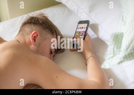 Ein Teenager Junge liegt im Bett und schläft mit seinem Handy Stockfoto