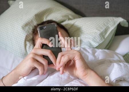 Ein Teenager Junge liegt im Bett mit seinem Handy Stockfoto