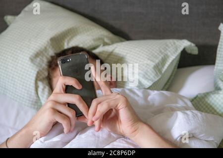Ein Teenager Junge liegt im Bett mit seinem Handy Stockfoto