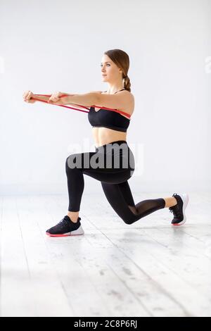 Frau tut ein Power-Band hinter Ausfallschritt und vorwärts Push-Übung, um ihre Kernmuskeln mit Widerstand in einem High-Key-Fitnessstudio mit Copyspace zu stärken Stockfoto