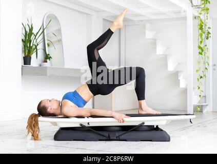 Junge Frau, die eine Surf-Single-Bridge Pose macht, um ihre Brust und Schultern in einer Seitenansicht in einem High-Key-Fitnessstudio in einem Gesundheits- und Fitnesskonzept zu öffnen Stockfoto