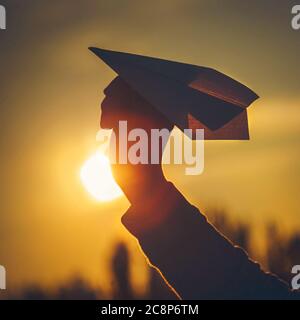 Papierflugzeug in der Hand des Menschen bei orangefarbenem Sonnenuntergang Stockfoto