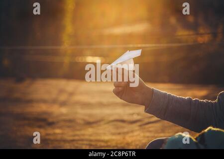 Papierflugzeug in der Hand des Menschen bei orangefarbenem Sonnenuntergang Stockfoto