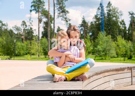 Zwei Schülerinnen sitzen auf einer Bank im Park und machen Hausaufgaben Stockfoto