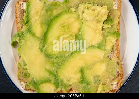 Frisch pürierte Avocado auf Vollkornbrot. Ein gesundes vegetarisches Sandwich auf einer strukturierten Steinoberfläche. Stockfoto