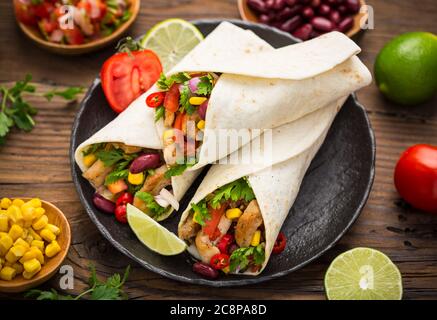 Frische Tortilla Wraps mit Hühnerfleisch und Gemüse auf dem Holztisch Stockfoto