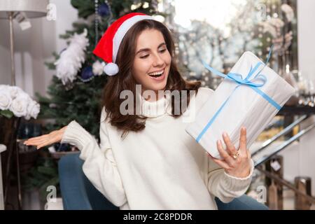 Aufgeregt junge Frau trägt Weihnachtsmütze, lachend, Blick auf Geschenk-Box in der Hand Stockfoto