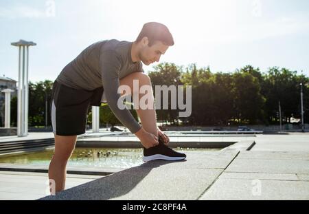 Start des Marathons. Junger, hübscher Mann, der Schnürsenkel auf Stufen bindet Stockfoto