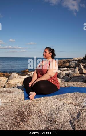 Frau am Meer sitzt auf einer Matte und atmet oder betet in nachdenklicher Reflexion Stockfoto