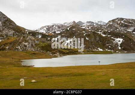 Wanderer rund um den Lago Ercina Gletschersee bei bewölktem Tag mit Schnee in den nahe gelegenen Gipfeln (Cangas de Onís, Nationalpark Picos de Europa, Asturien, Spanien) Stockfoto