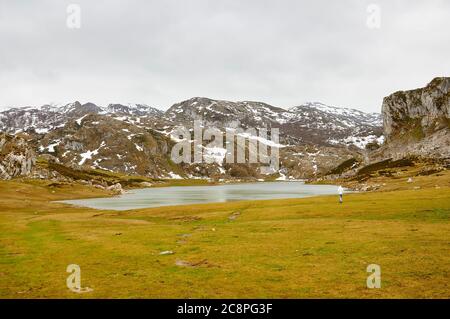 Wanderer am Lago Ercina Gletschersee bei bewölktem Tag mit Schnee auf den umliegenden Gipfeln (Cangas de Onís, Nationalpark Picos de Europa, Asturien, Spanien) Stockfoto