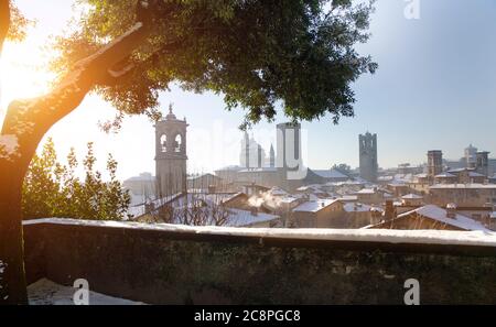 Blick über eine niedrige Wand auf die schneebedeckten Dächer und Türme in der Citta Alta Gegend von Bergamo, Italien Stockfoto