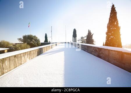 Eine schneebedeckte Straße mit der Sonne beleuchtet Wände und Tannen auf beiden Seiten. Stockfoto