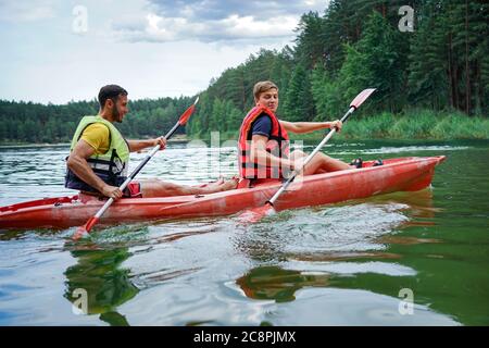 Zwei Jungs in einem roten Kajak auf dem Fluss, in Schwimmwesten Stockfoto