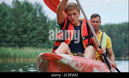 Zwei Jungs in einem roten Kajak auf dem Fluss, in Schwimmwesten Stockfoto