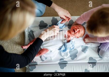 Mutter und Tochter tendieren dazu, Baby auf der Wickelmatte zu weinen Stockfoto