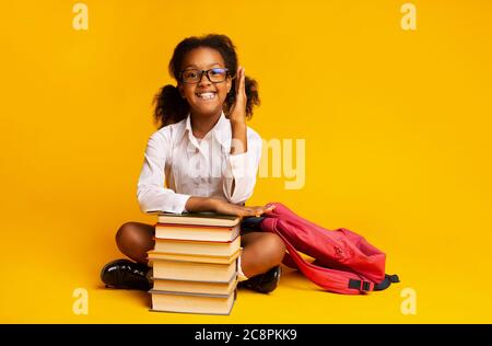 African Schoolgirl Heben Hand Sitzen Bei Bücher Über Gelben Hintergrund Stockfoto