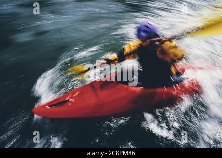 Lange Exposition von weiblichen Wildwasser Kajakfahrer paddeln Stromschnellen und surfen auf einem schnell fließenden Fluss. Stockfoto