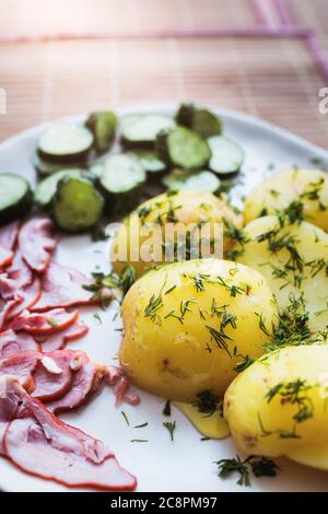 Frisch geerntete junge gekochte Kartoffeln mit Dill und Butter - Speck und Gurke als Snack Stockfoto