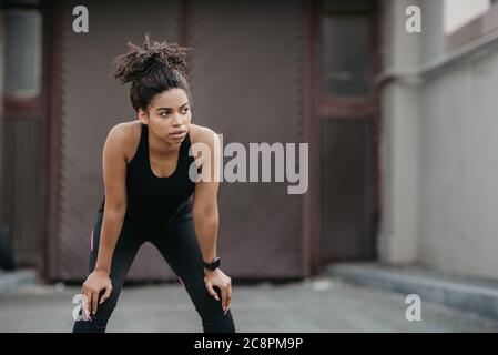 Ruhen Sie sich während des Trainings im Freien aus. afroamerikanisches Mädchen mit Fitness-Tracker Entspannung vom Joggen Stockfoto