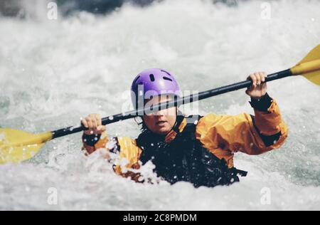 Wildwasser-Kajakfahrerin paddelt Stromschnellen und surft auf einem schnell fließenden Fluss. Stockfoto