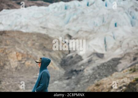 Eine junge Frau, die am Ende eines Gletschers an einer felsigen Küste in Alaska steht. Stockfoto