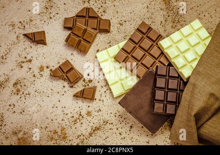 Schokoladen-Süßigkeiten. Schokoriegel in Sackleinen. Verschiedene Milch und dunkle Schokolade. Schokoladenstücke auf Holzhintergrund. Stockfoto