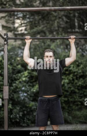 Junger Mann tut Pull-up auf horizontale Bar. Mans Fitness im Stadion Stockfoto