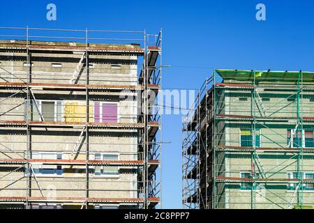 Gerüste, die eine Fassade eines Wohngebäudes bedecken, das in Renovierung auf einem blauen Himmel Hintergrund steht Stockfoto