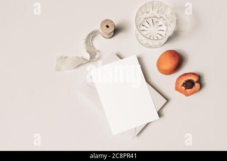 Sommerhochzeit Stillleben. Glas Wasser, Cocktail, Aprikosenfrüchte und Seidenband auf beigem Tischhintergrund. Leere Grußkarte – Szene im Nachbau Stockfoto