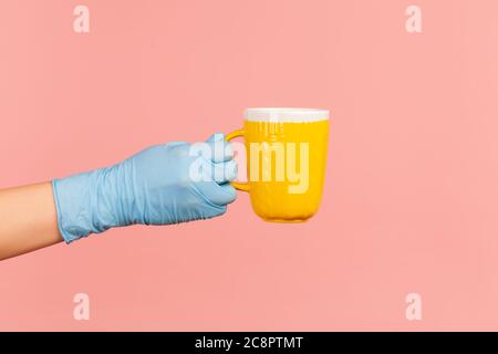Profil Seitenansicht Nahaufnahme der menschlichen Hand in blauen OP-Handschuhen halten und zeigt gelbe Tasse heißen Drink in der Hand. Indoor, Studio-Aufnahme, isoliert auf Stockfoto