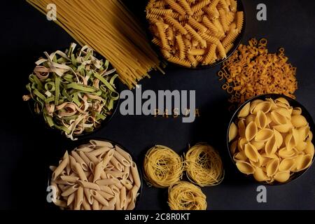 Rohe runde Pasta auf dunklem Hintergrund. Das Wort PASTA aus Holzbuchstaben in der Mitte. Das Konzept der köstlichen Speisen. Draufsicht, flaches Layout, Kopie Stockfoto
