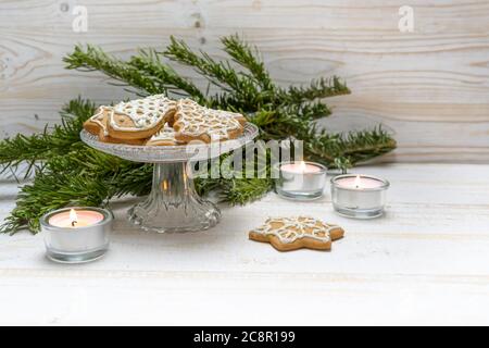 Lebkuchen zu Weihnachten auf einer Kristallglas-Schale, brennende Kerzen und Tannenzweige auf einem weiß bemalten Holztisch, Kopierraum, ausgewählte Focu Stockfoto